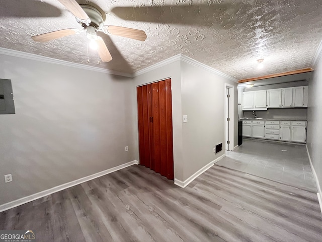 spare room featuring ceiling fan, a textured ceiling, crown molding, electric panel, and light wood-type flooring