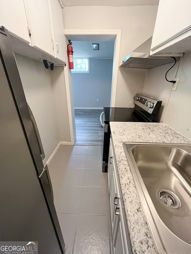 kitchen with light stone counters, stainless steel fridge, light tile patterned floors, sink, and white cabinets