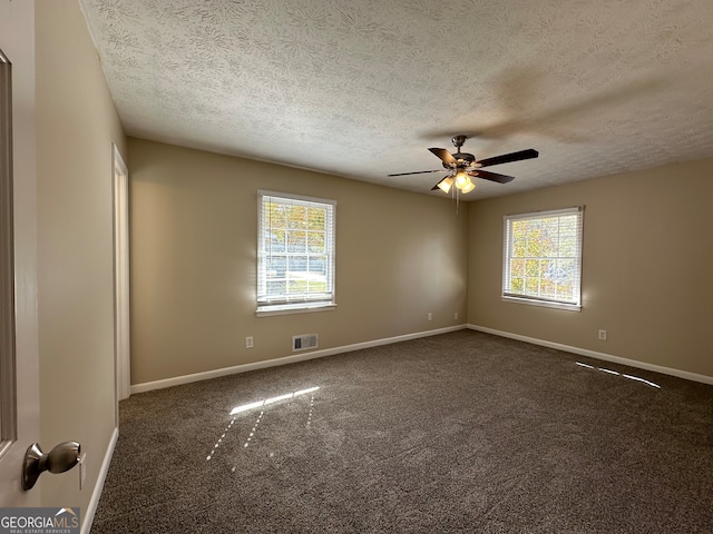 empty room featuring ceiling fan, a textured ceiling, and dark carpet