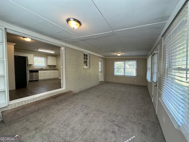 unfurnished living room with a wealth of natural light, brick wall, sink, and dark carpet