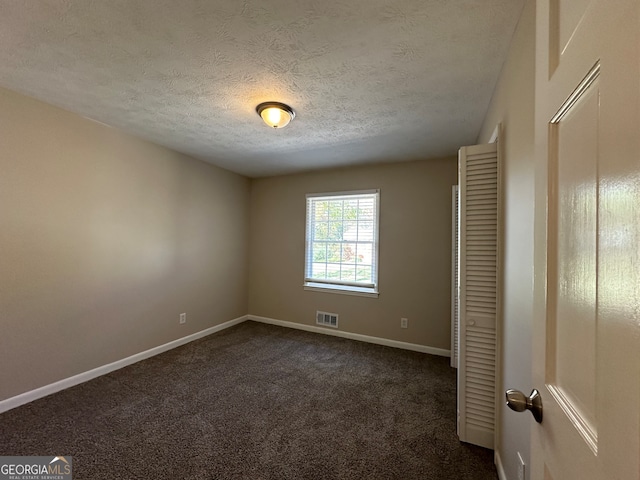 spare room with a textured ceiling and dark carpet