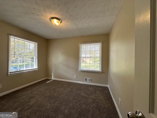 spare room with a textured ceiling, dark colored carpet, and a healthy amount of sunlight