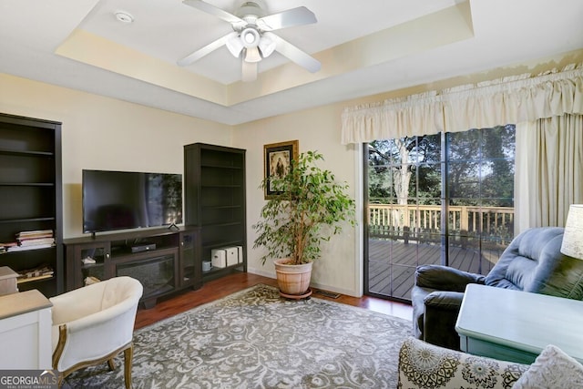 living room featuring ceiling fan, wood-type flooring, and a raised ceiling