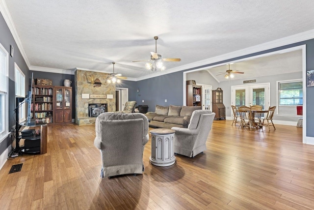 living room with a stone fireplace, ornamental molding, and light wood-type flooring