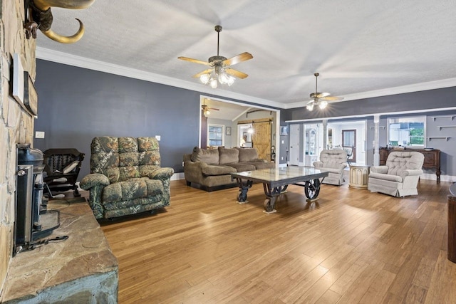 living room with ceiling fan, a barn door, hardwood / wood-style floors, a textured ceiling, and ornamental molding