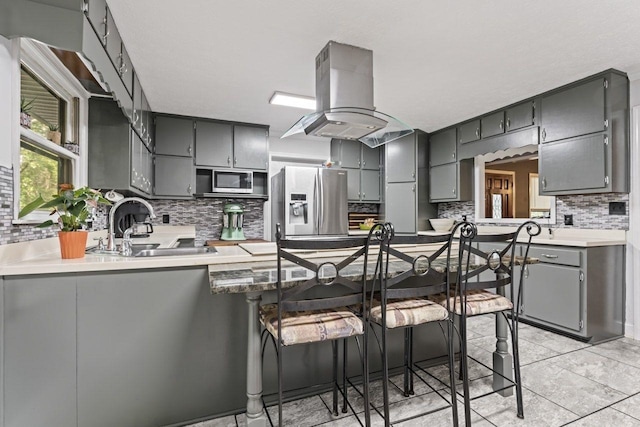 kitchen with kitchen peninsula, appliances with stainless steel finishes, island range hood, and gray cabinets