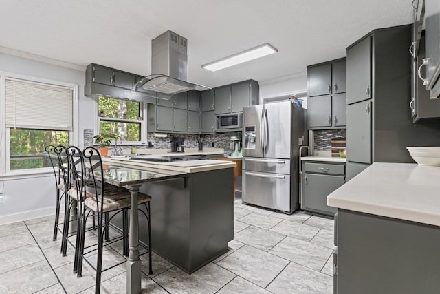 kitchen featuring appliances with stainless steel finishes, tasteful backsplash, ornamental molding, island range hood, and a kitchen island