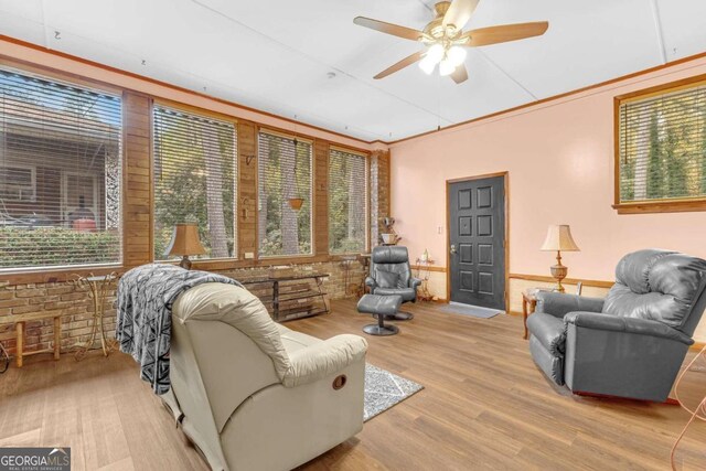 sitting room featuring light hardwood / wood-style floors, ceiling fan, and brick wall