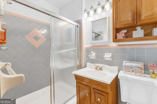 bathroom featuring tile walls, backsplash, vanity, toilet, and a shower with shower door