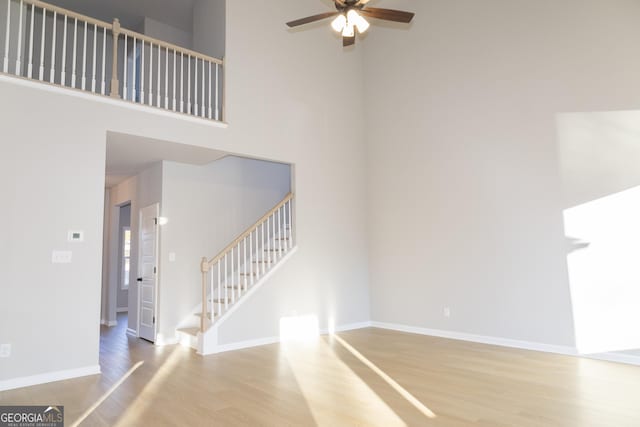 unfurnished living room with ceiling fan, a high ceiling, and light wood-type flooring