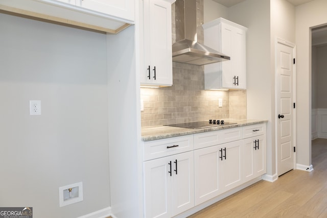 kitchen featuring white cabinetry, wall chimney range hood, light stone counters, black electric cooktop, and light wood-type flooring