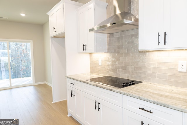 kitchen with white cabinets, light hardwood / wood-style flooring, wall chimney exhaust hood, light stone countertops, and black electric cooktop