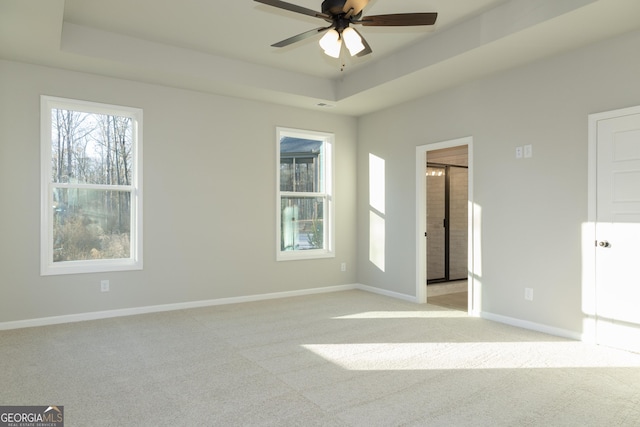 unfurnished room featuring light carpet, a tray ceiling, and ceiling fan