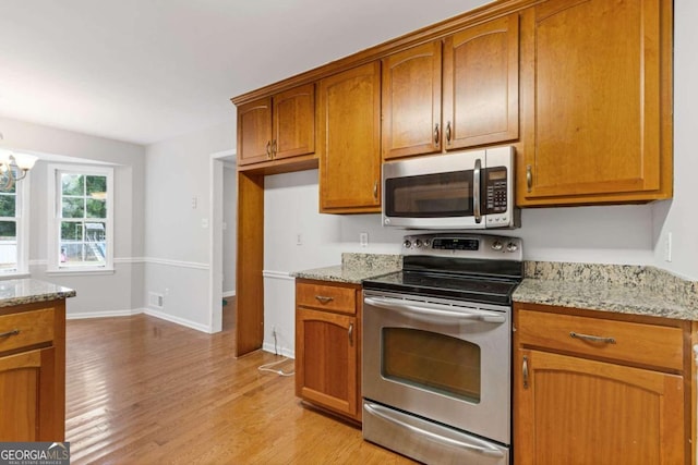 kitchen featuring light wood-type flooring, an inviting chandelier, light stone counters, and stainless steel appliances