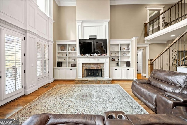 living room with a fireplace, a towering ceiling, light hardwood / wood-style flooring, and crown molding