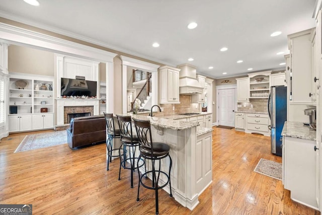 kitchen with light stone counters, appliances with stainless steel finishes, ornamental molding, light hardwood / wood-style flooring, and white cabinets