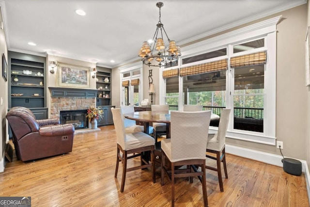 living room featuring a stone fireplace, built in features, ornamental molding, and light hardwood / wood-style flooring