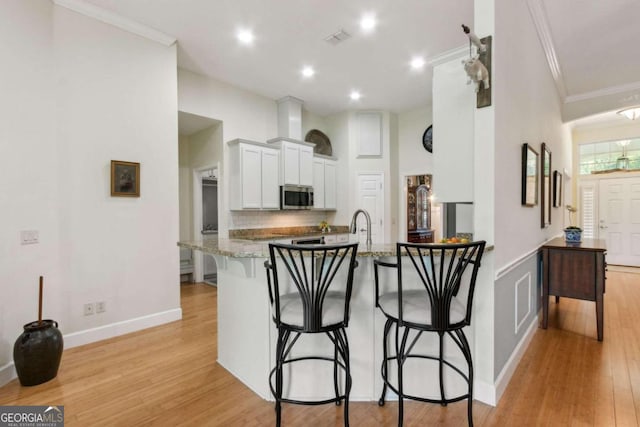 kitchen featuring light stone counters, white cabinetry, light wood-type flooring, a kitchen bar, and kitchen peninsula