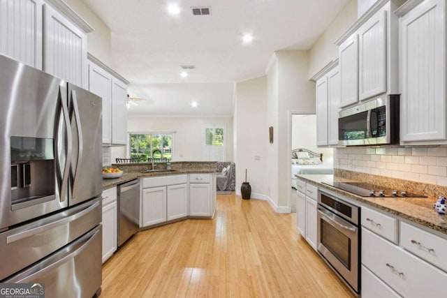 kitchen with stainless steel appliances, white cabinetry, sink, ornamental molding, and light hardwood / wood-style flooring