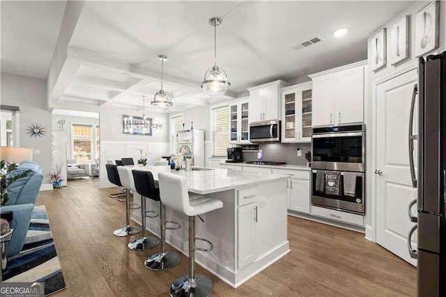 kitchen with stainless steel appliances, wood-type flooring, white cabinets, and an island with sink