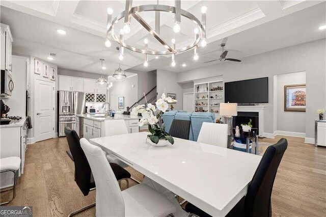 dining area featuring sink, ceiling fan with notable chandelier, beam ceiling, light hardwood / wood-style flooring, and crown molding