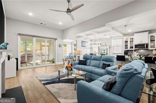 living room featuring light wood-type flooring, ceiling fan with notable chandelier, beam ceiling, and coffered ceiling