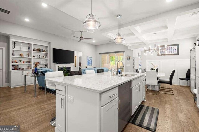 kitchen with white cabinets, light wood-type flooring, dishwasher, and an island with sink