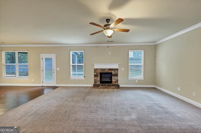 unfurnished living room featuring ceiling fan, a stone fireplace, crown molding, and dark carpet