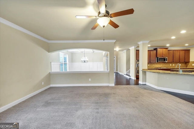 unfurnished living room featuring ceiling fan with notable chandelier, dark carpet, and ornamental molding