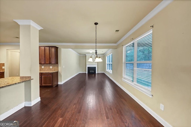 unfurnished living room with dark wood-type flooring, an inviting chandelier, and crown molding