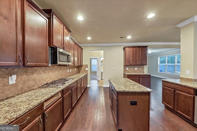 kitchen with dark hardwood / wood-style flooring, a center island, backsplash, light stone countertops, and appliances with stainless steel finishes