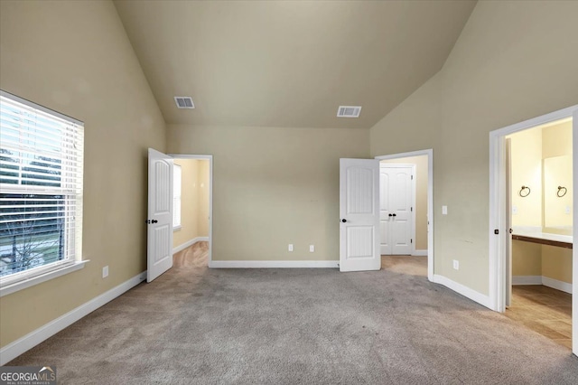 unfurnished bedroom featuring high vaulted ceiling, light colored carpet, and ensuite bath