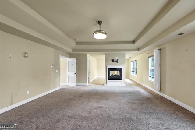 unfurnished living room featuring a multi sided fireplace, light carpet, and a raised ceiling