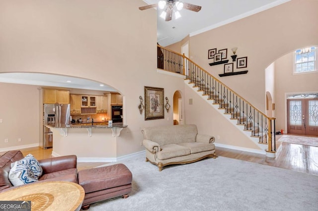 living room with ceiling fan, crown molding, light hardwood / wood-style floors, and a towering ceiling