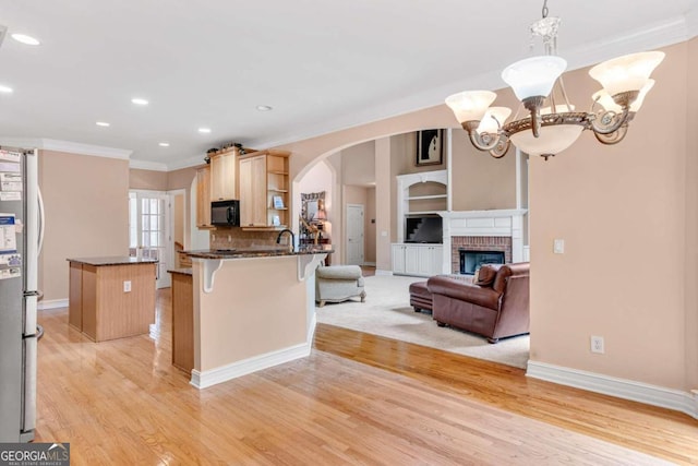 kitchen featuring a breakfast bar, a fireplace, light hardwood / wood-style flooring, stainless steel fridge, and pendant lighting