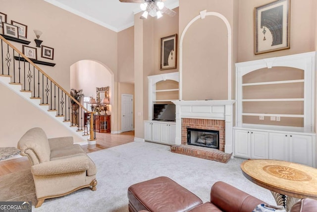 living room featuring a high ceiling, light hardwood / wood-style floors, ornamental molding, a fireplace, and built in features