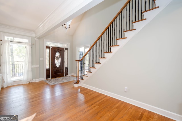 foyer entrance featuring ornamental molding, a high ceiling, an inviting chandelier, and wood-type flooring