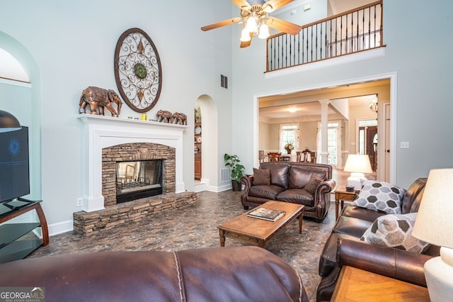 living room featuring a fireplace, ceiling fan, a high ceiling, and decorative columns