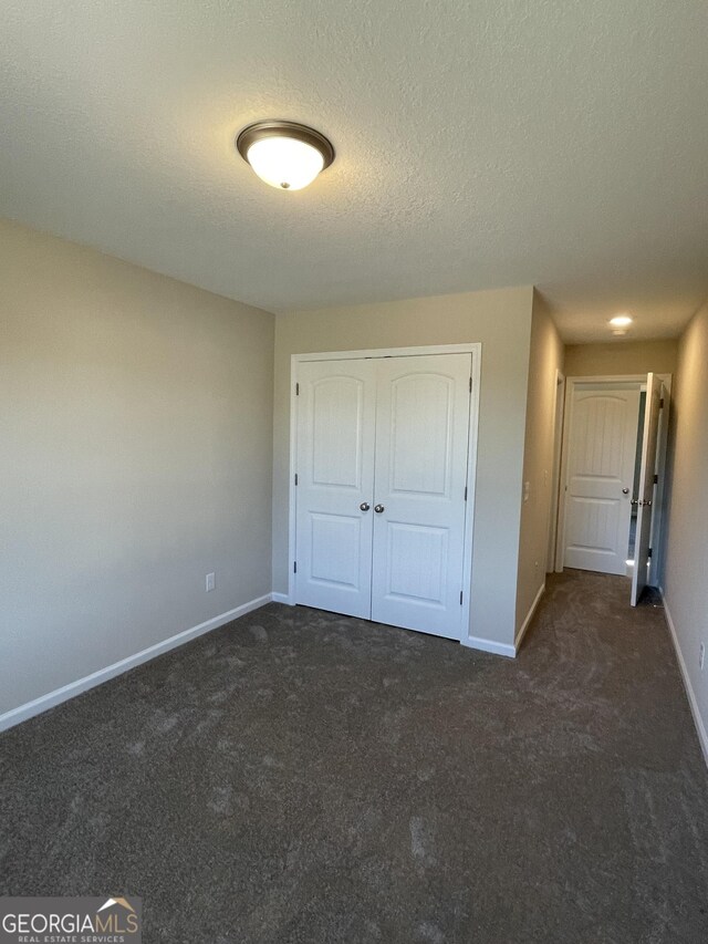 unfurnished bedroom with dark colored carpet, a textured ceiling, and a closet