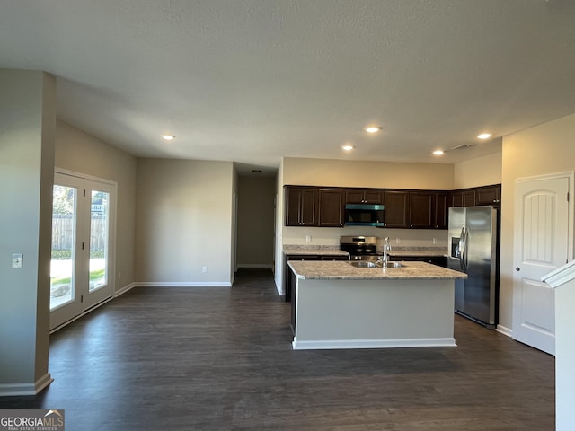 kitchen with stainless steel appliances, light stone counters, dark hardwood / wood-style flooring, an island with sink, and dark brown cabinets