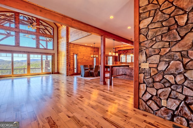 unfurnished living room with a mountain view, ceiling fan with notable chandelier, light hardwood / wood-style floors, and wood walls