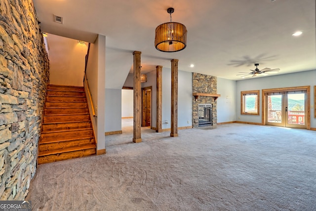 unfurnished living room with carpet flooring, french doors, ceiling fan, and a stone fireplace