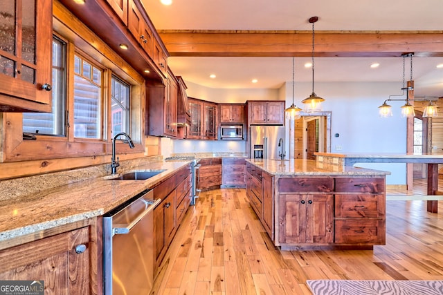 kitchen with stainless steel appliances, a kitchen island, decorative light fixtures, light stone countertops, and light hardwood / wood-style floors