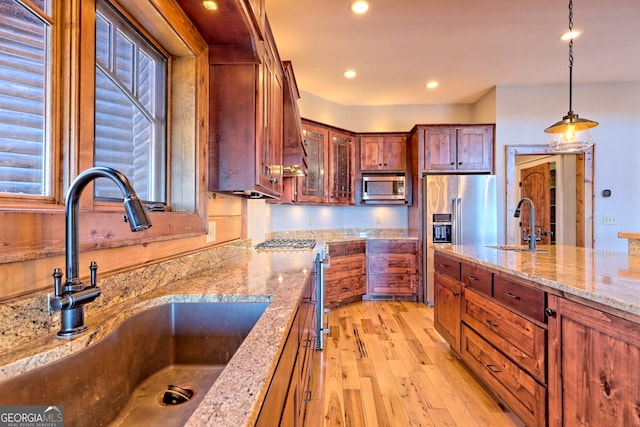 kitchen with high end appliances, light wood-type flooring, sink, and decorative light fixtures