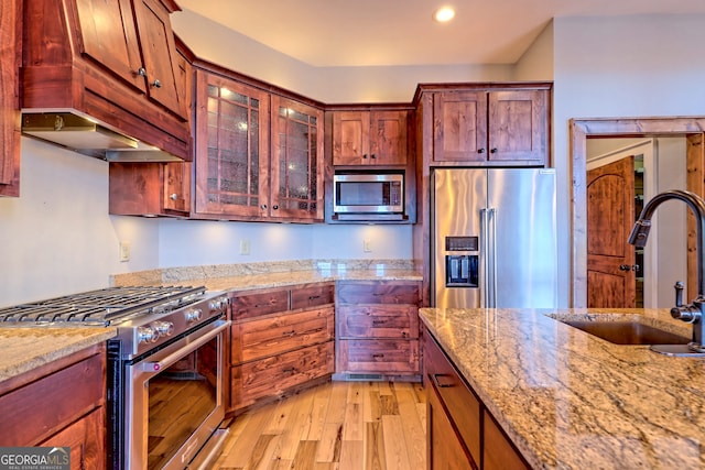 kitchen featuring light wood-type flooring, high quality appliances, light stone counters, and sink