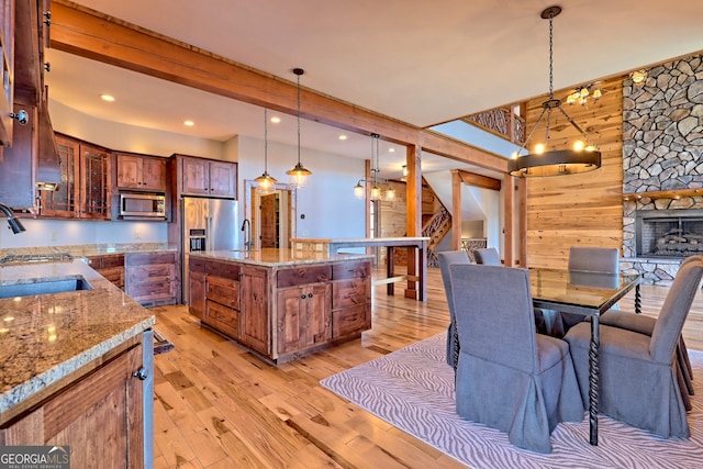 kitchen with light stone counters, pendant lighting, appliances with stainless steel finishes, and light hardwood / wood-style flooring