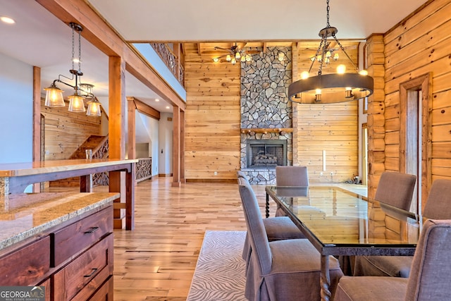 dining area featuring a chandelier, a fireplace, wooden walls, and light hardwood / wood-style flooring