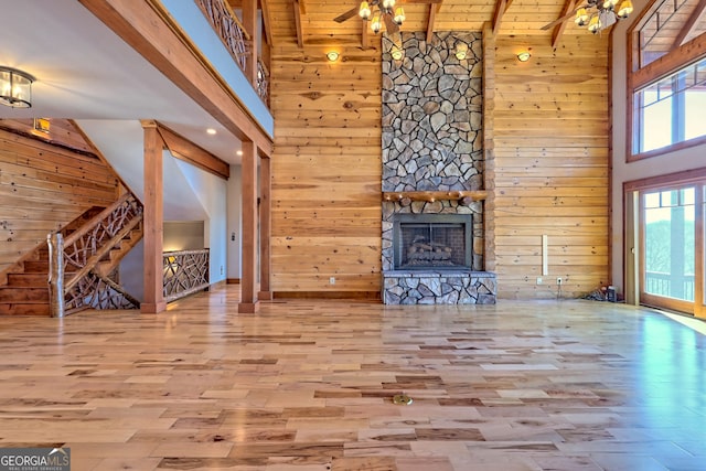 unfurnished living room featuring light wood-type flooring, wood walls, beamed ceiling, and high vaulted ceiling