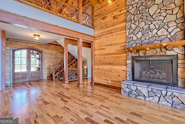 unfurnished living room with wooden walls, wood-type flooring, french doors, and a fireplace