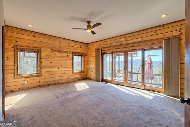 carpeted empty room featuring a mountain view, ceiling fan, plenty of natural light, and wooden walls